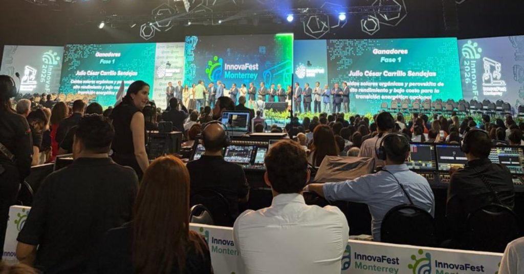 Conference stage at InnovaFest Monterrey with a line of presenters and teal screens behind them; audience and tech staff visible in foreground.